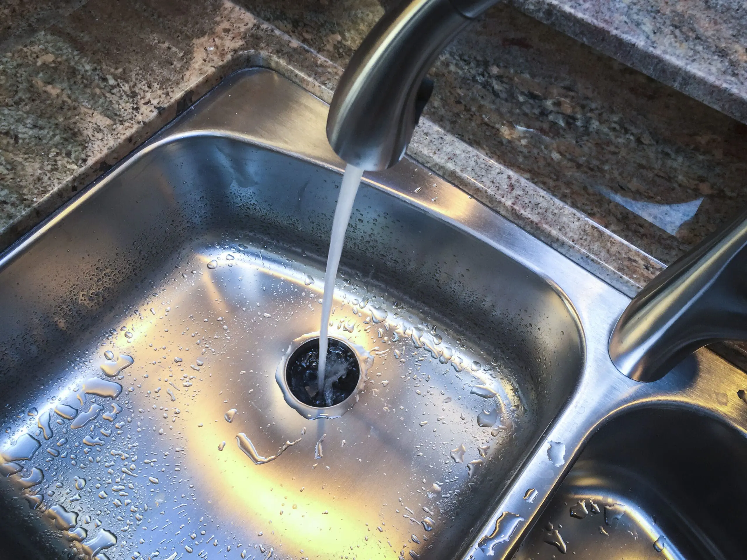 Stainless steel sink with garbage disposal. Water is running.