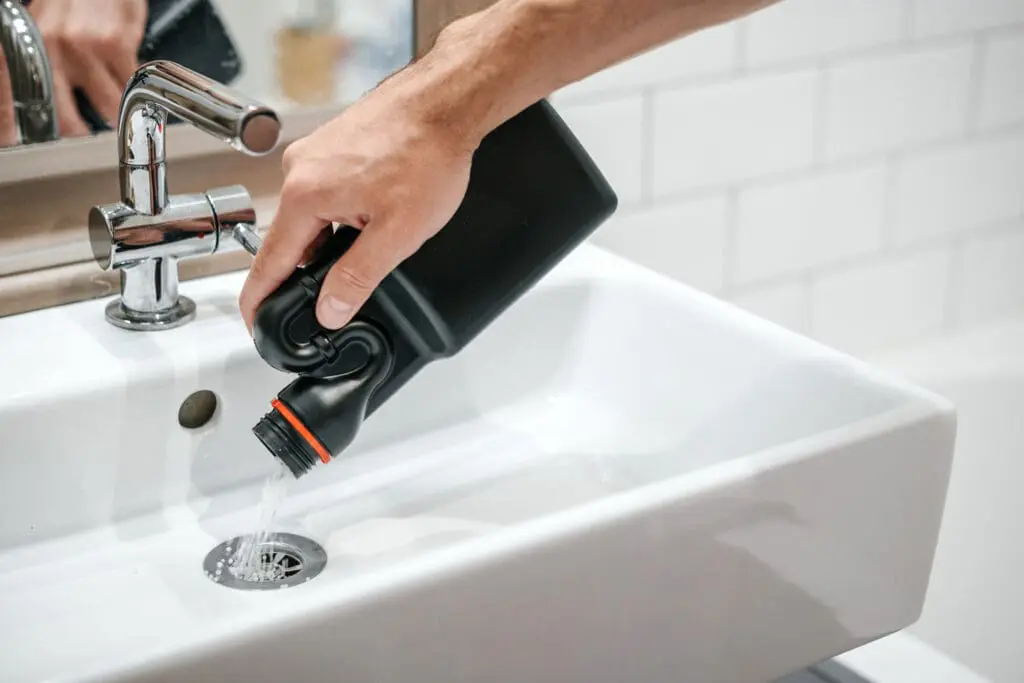 Removal of blockage in the sink, the hand of a man with a bottle of a special remedy with granules