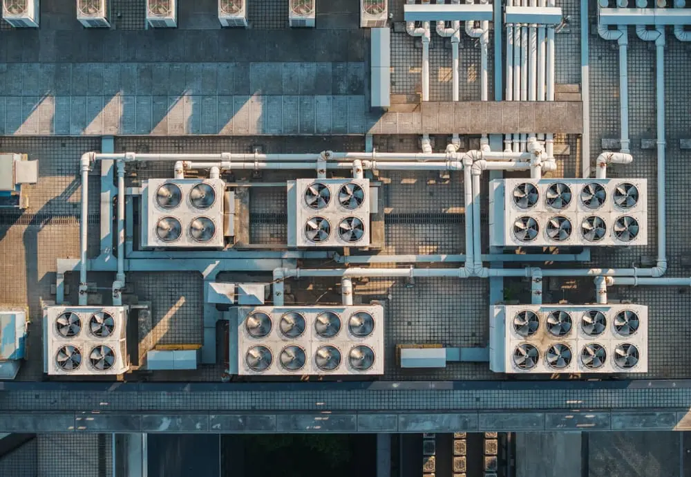 Aerial view of multiple cooling units situated on a rooftop. The system features a series of large HVAC units and extensive piping. rooftop hvac installation