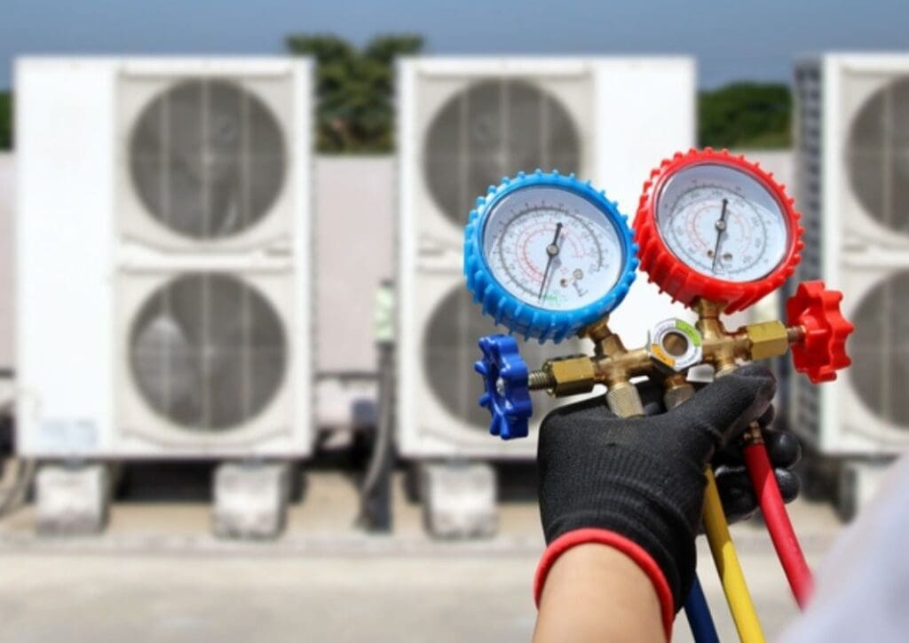 Electrical conditioning service technician using measuring manifold gauge checking HVAC condition system and refrigerant filling air conditioner after cleaning and maintenance compressor units.