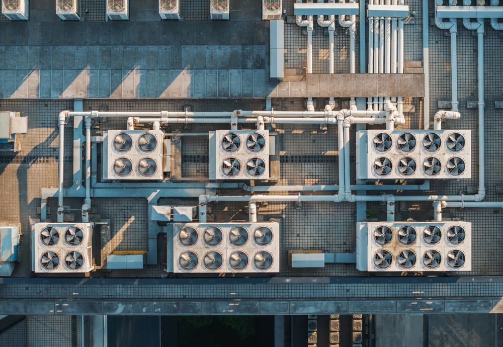 Aerial view of multiple cooling units situated on a rooftop. The system features a series of large HVAC units and extensive piping.