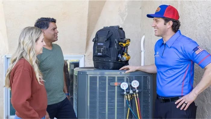 This image shows AC installation in Lehi UT with a technician from Western Heating, Air & Plumbing speaking with homeowners next to an outdoor condenser unit. The technician explains installation details and system performance while tools and gauges are visible on the unit. The homeowners listen and ask questions, showing a clear service interaction during the installation process. Western Heating, Air & Plumbing provides air conditioning installation in Lehi Utah, helping homeowners understand their system and maintain indoor comfort with reliable service and clear communication.