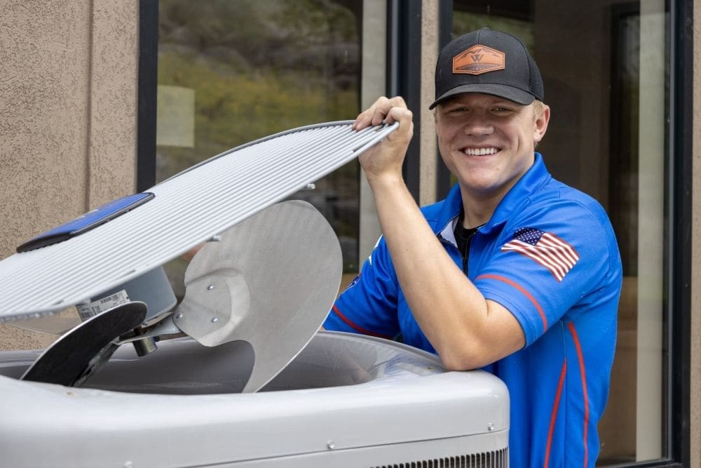 A professional HVAC technician from Western Heating, Air & Plumbing performs AC maintenance in Lehi UT by opening and inspecting an outdoor condenser unit. The technician checks internal components such as the fan blades and coils to confirm proper system function and airflow. This residential air conditioning service in Lehi UT supports system performance, lowers energy use, and helps prevent breakdowns during peak summer heat. Western Heating, Air & Plumbing, serving Utah County including Lehi, provides reliable AC maintenance services with experienced technicians focused on safe and effective system care.